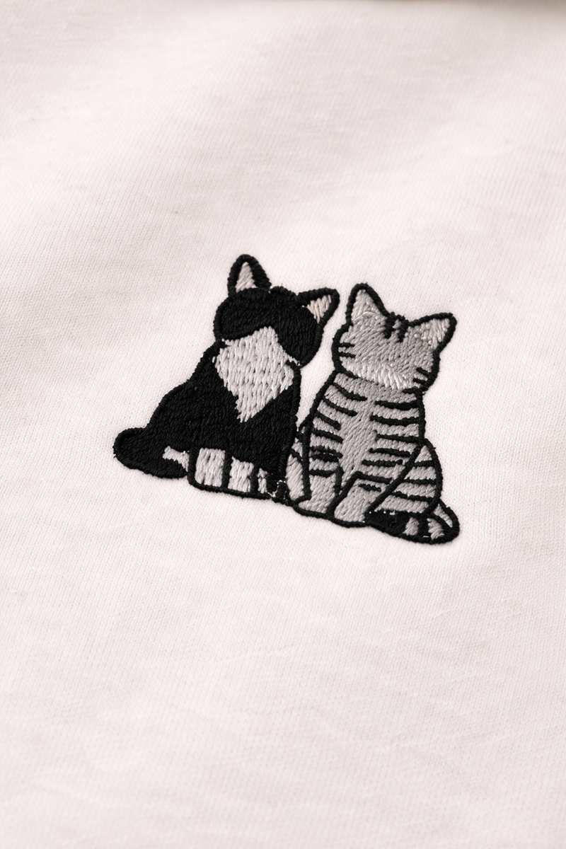 Embroidered design of two cats on a white fabric background